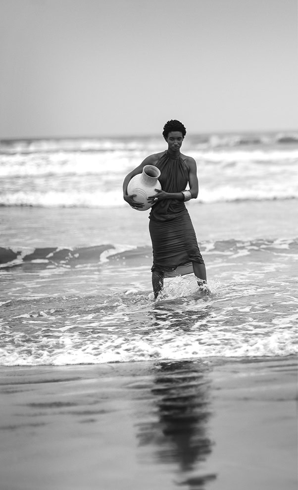 Vendedora de cerâmicas na praia com o mar ao fundo, fotografia artística em preto e branco destacando cultura e tradição.