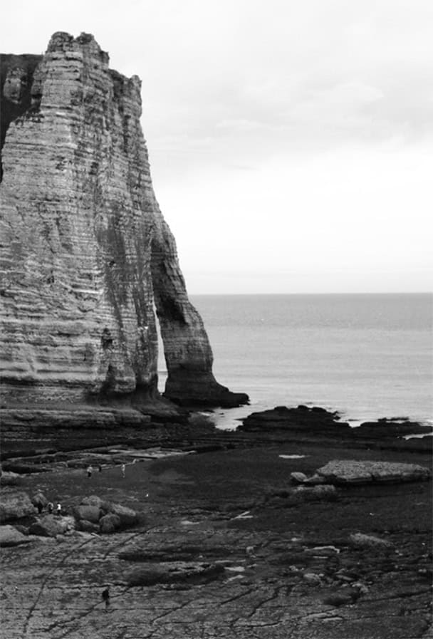 Falésias de calcário imponentes na costa, formando uma paisagem dramática e atraente no cenário marítimo. Fotografia em preto e branco capturando a beleza natural das formações rochosas e o mar ao fundo.