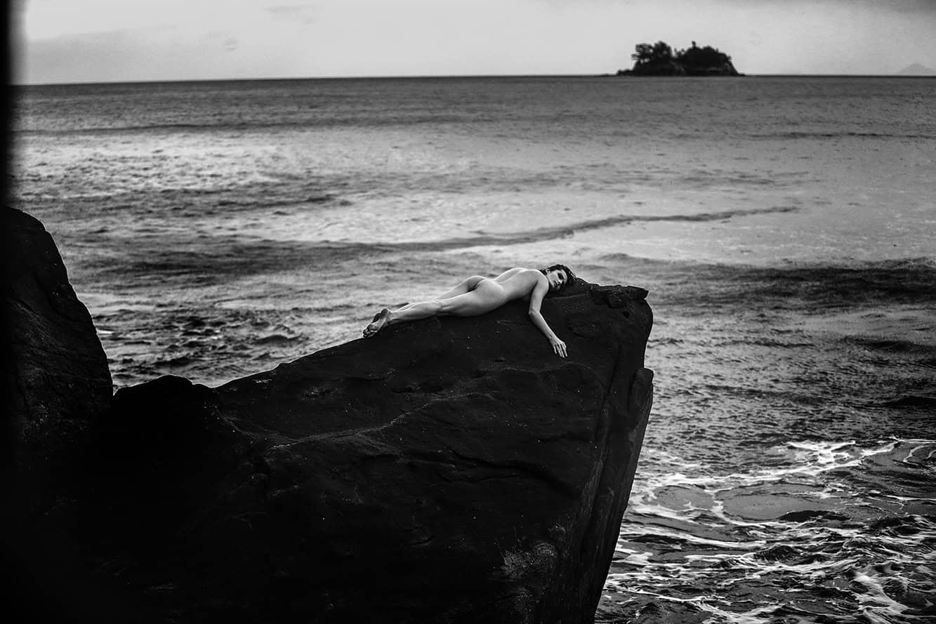Risco com mulher deitada sobre uma pedra na praia em fotos de ensaio fotográfico black and white, estilo artístico e retrato de moda na natureza, símbolo de beleza e expressão artística.